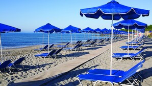 Una spiaggia con file di sdraio blu e ombrelloni abbinati, una passerella in legno e l'oceano sullo sfondo.