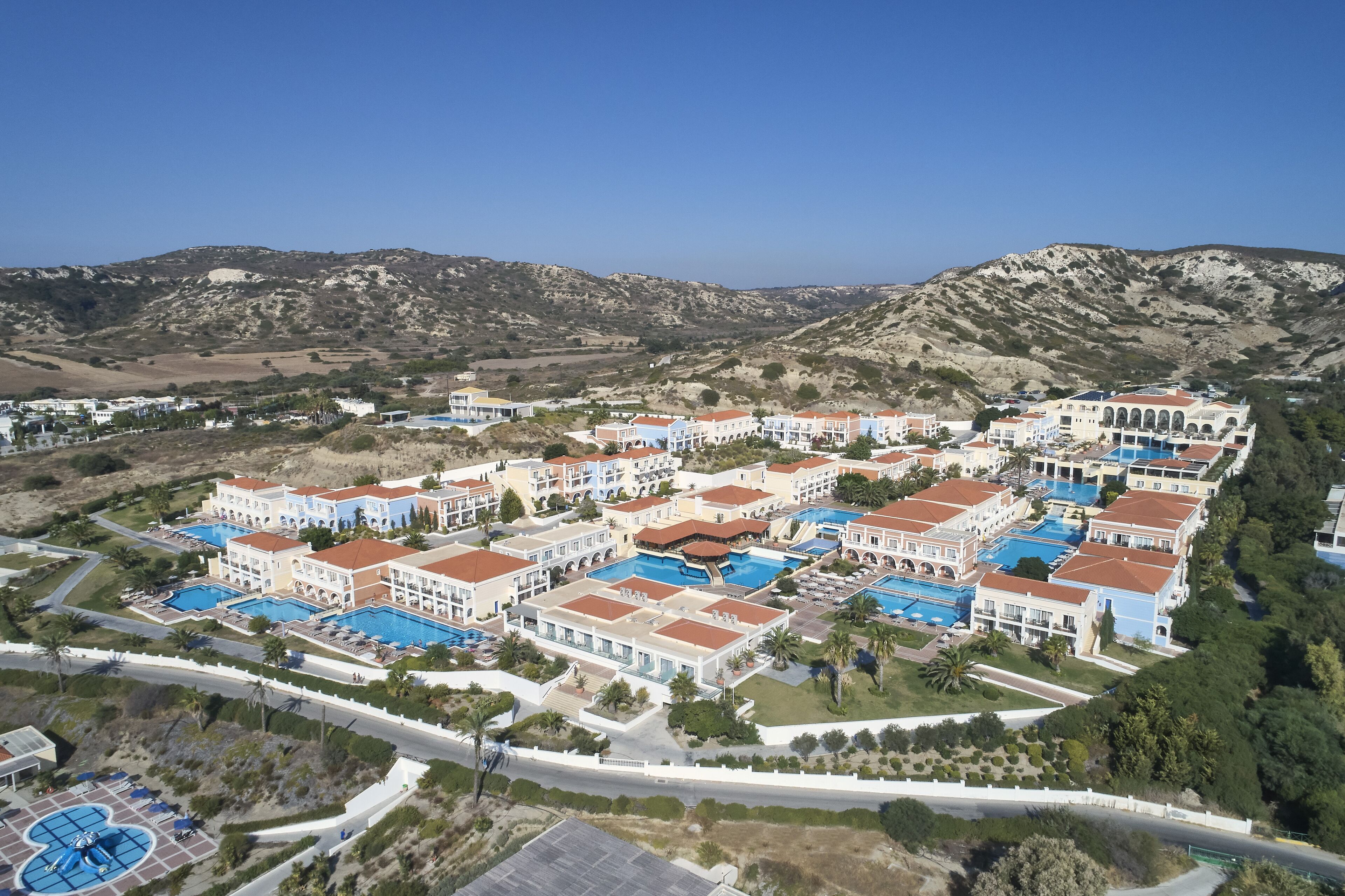 A resort with multiple buildings, swimming pools, and a mountainous backdrop.