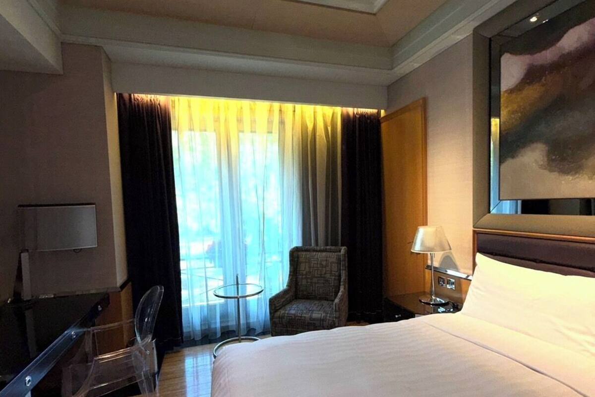A hotel room with a large bed, a desk, a chair, a small table, and a painting on the wall.