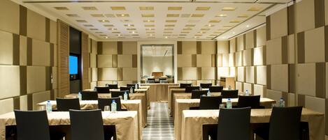 Un salón de conferencias con mesas y sillas, una pantalla grande y una mesa larga con mantel.