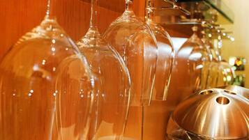 A collection of clear wine glasses hanging from a bar area, with a metal container and patterned mugs on the counter.