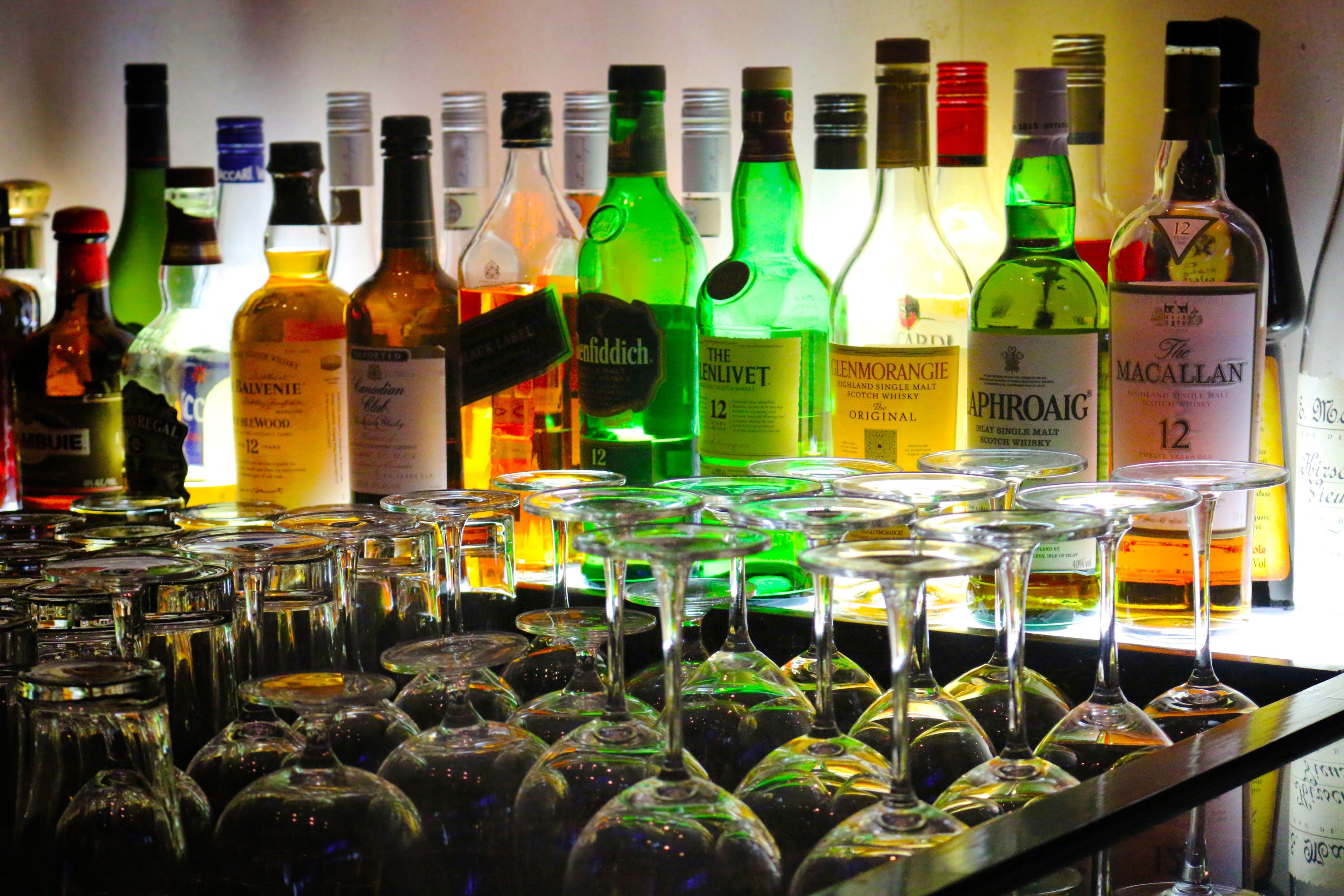 A bar with various bottles of alcohol and numerous empty wine glasses.