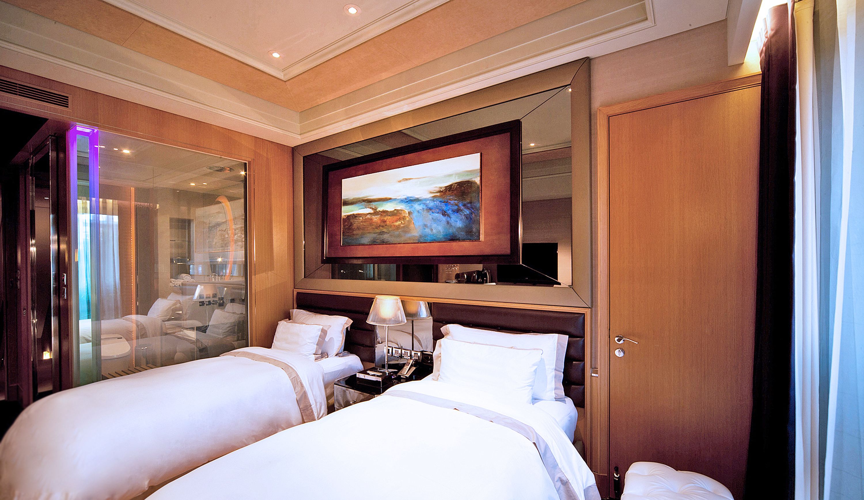 Habitación de hotel con dos camas, un televisor grande montado en la pared y una puerta de vidrio que da a un balcón.