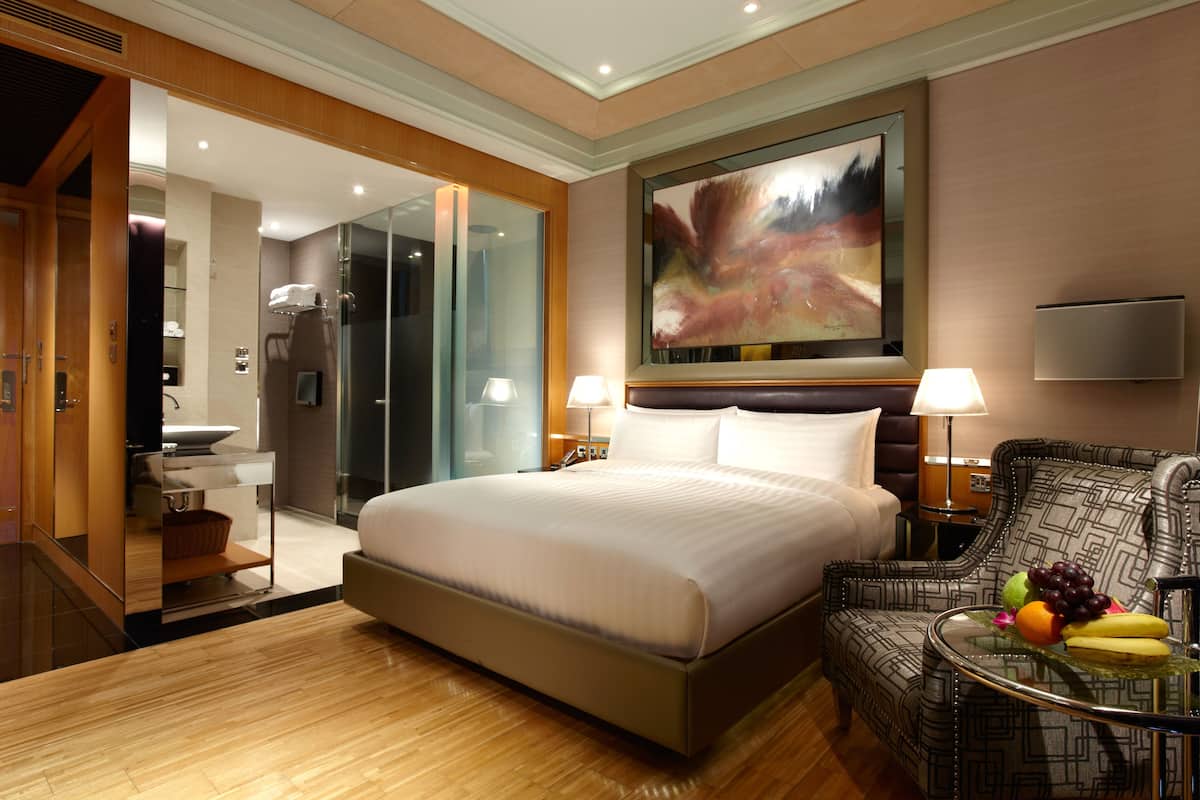 A modern hotel room with a large bed, a sitting area with a table, and a bathroom visible through an open door.