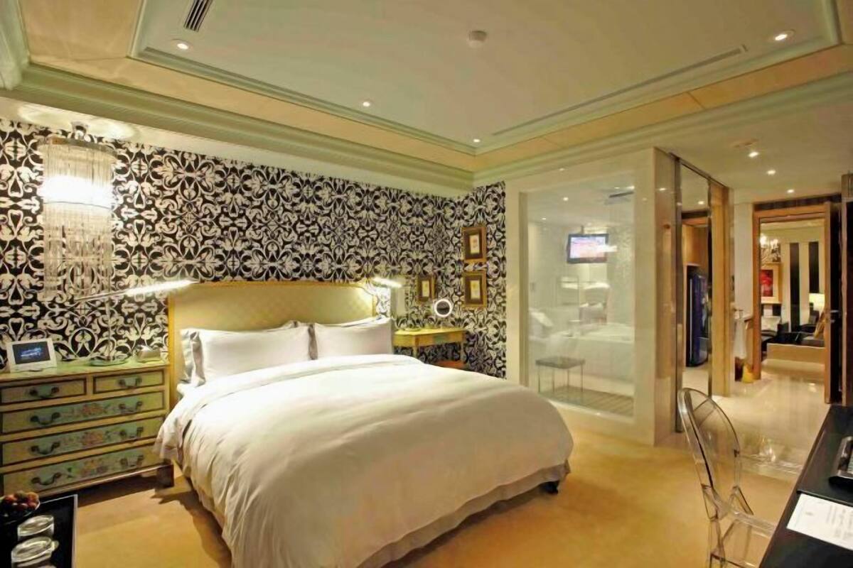A hotel room with a large bed, a nightstand, a wall-mounted TV, and a glass partition.