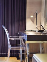 Een hotelkamer met een bureau, een transparante stoel, een lamp en een bed.