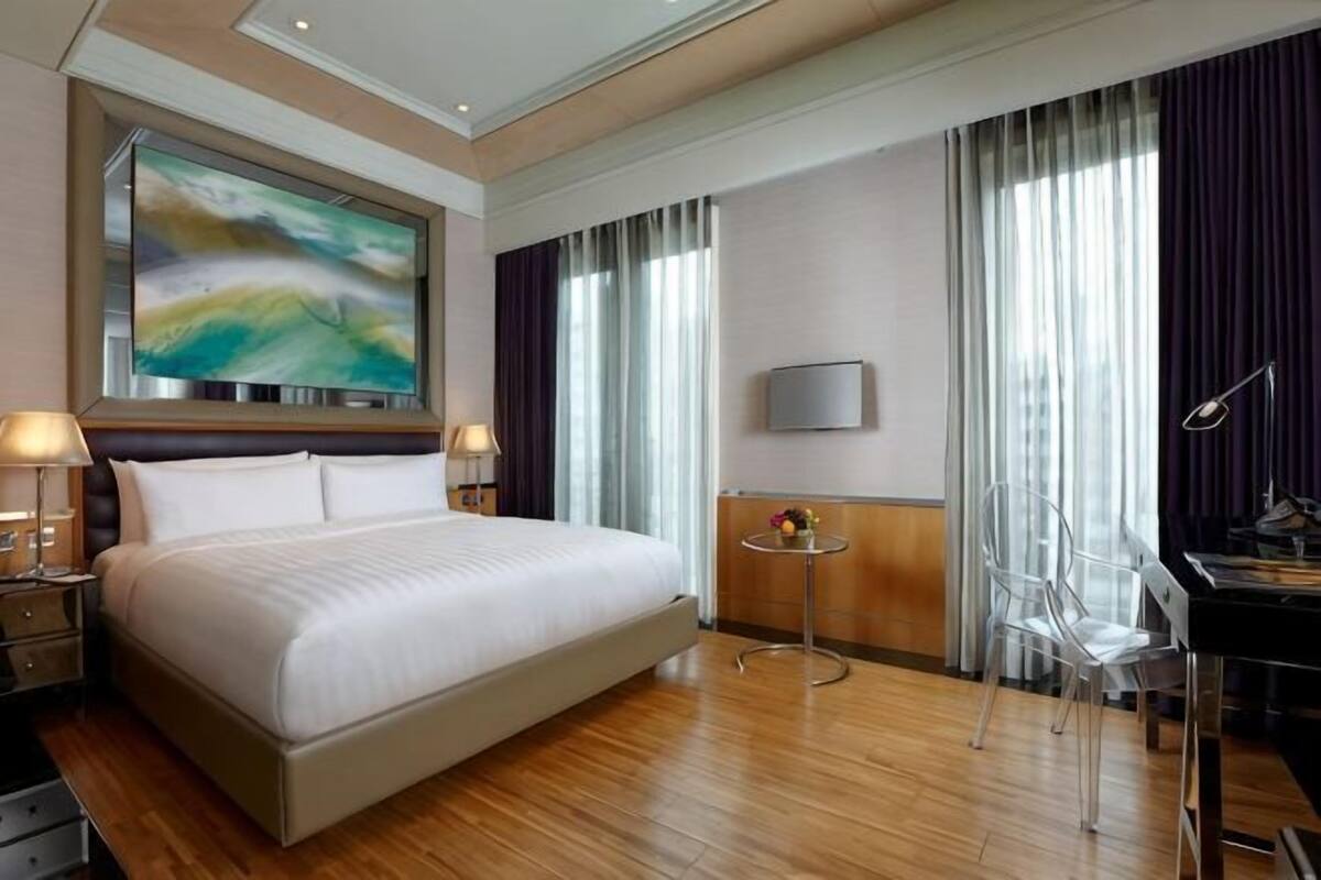 A hotel room with a large bed, a desk with a chair, a small table, and a painting on the wall.