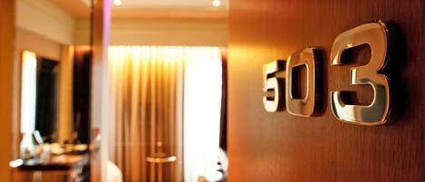 Interior de un hotel con un cartel con el número '503' en la pared, suelo de madera y una persona caminando al fondo.