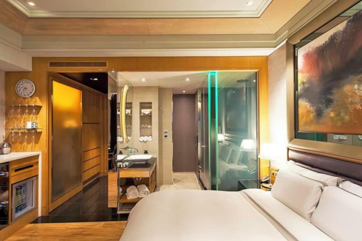 Una habitación de hotel con cama, baño, tocador y mampara de vidrio.