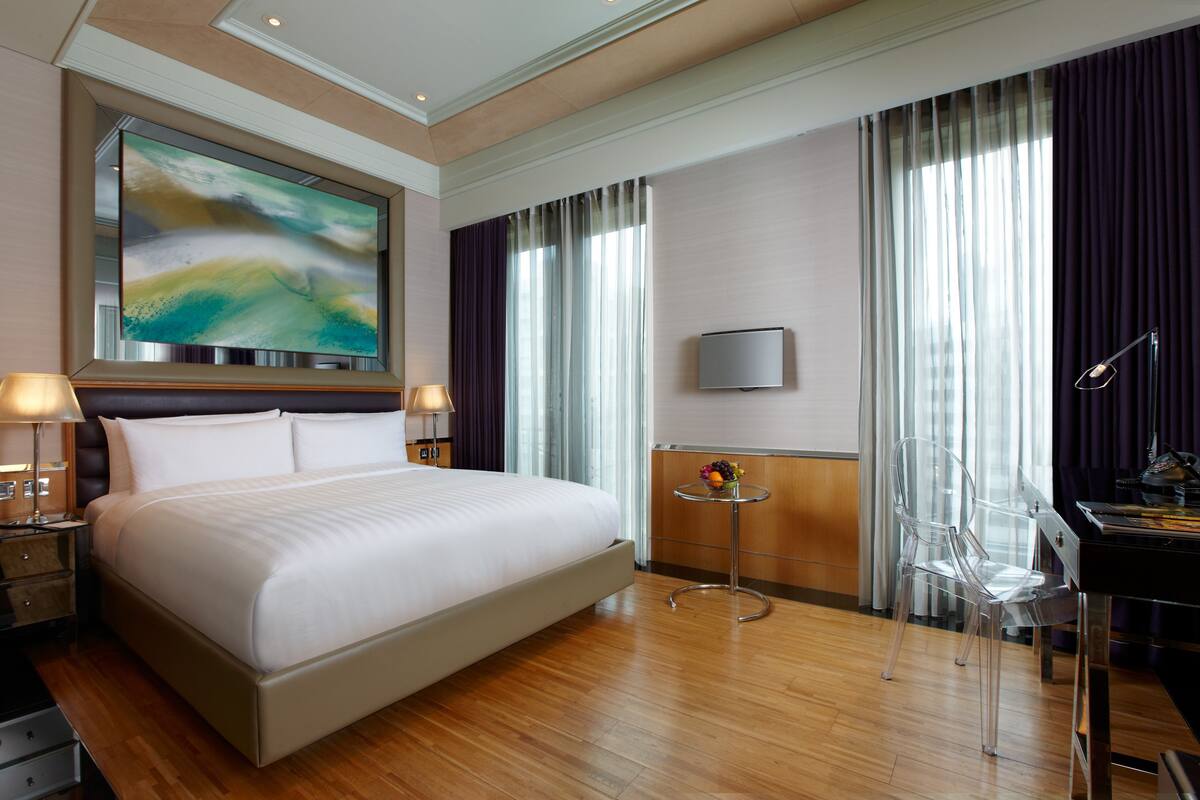 A modern hotel room with a large bed, a flat-screen TV, a desk with a chair, and a painting on the wall.