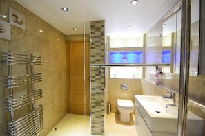 Een moderne badkamer met een douchecabine van glas, een wit toilet en een grote wastafel met spiegel.
