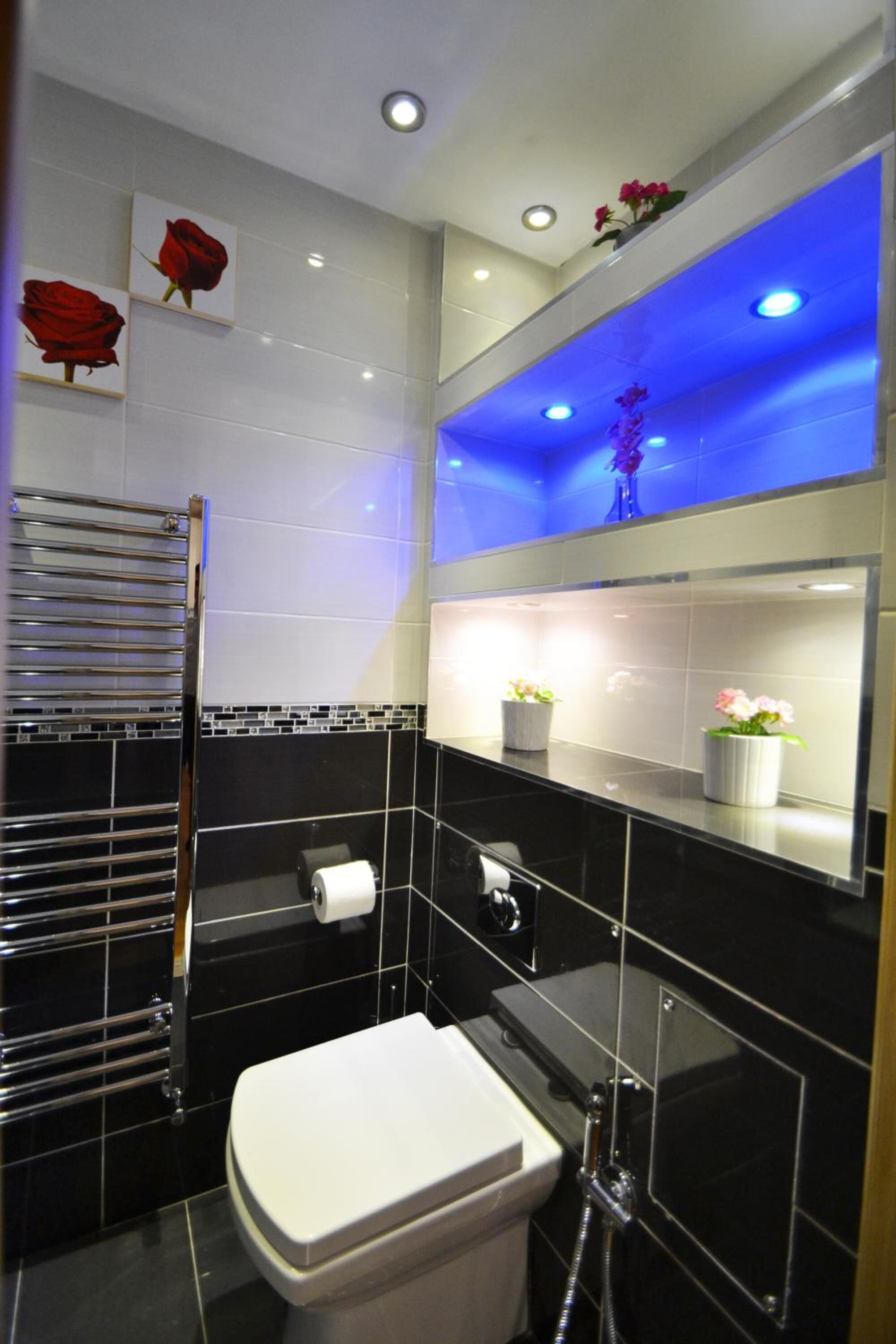 A modern bathroom with a black and white tiled design, a white toilet, a towel rack, and a shelf with potted plants.