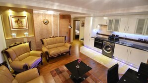 A spacious living room with a sofa set and a coffee table, a kitchen with modern appliances, and a separate bedroom visible through an open door.