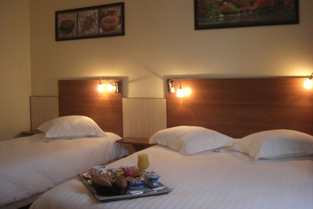 Habitación de hotel con dos camas, cada una con cabecera de madera y mesita de noche. Hay lámparas de pared sobre las camas y una bandeja con artículos para el desayuno sobre la cama.