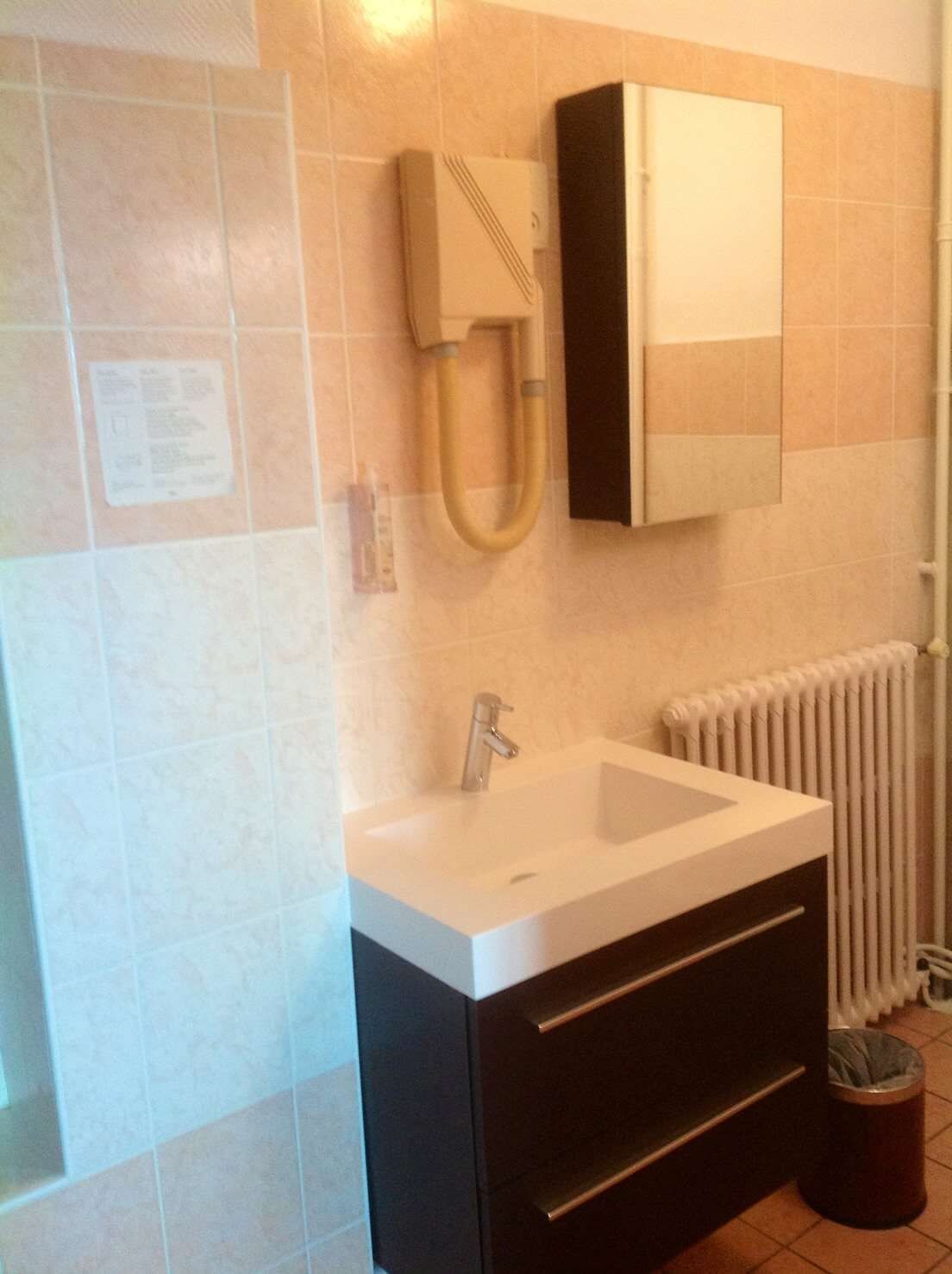 A bathroom with a white sink, a black cabinet, a towel rack, and a radiator.