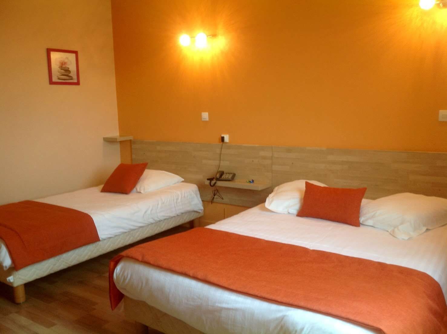 Een hotelkamer met twee bedden, elk voorzien van witte lakens en oranje sierkussens, en een houten hoofdbord.