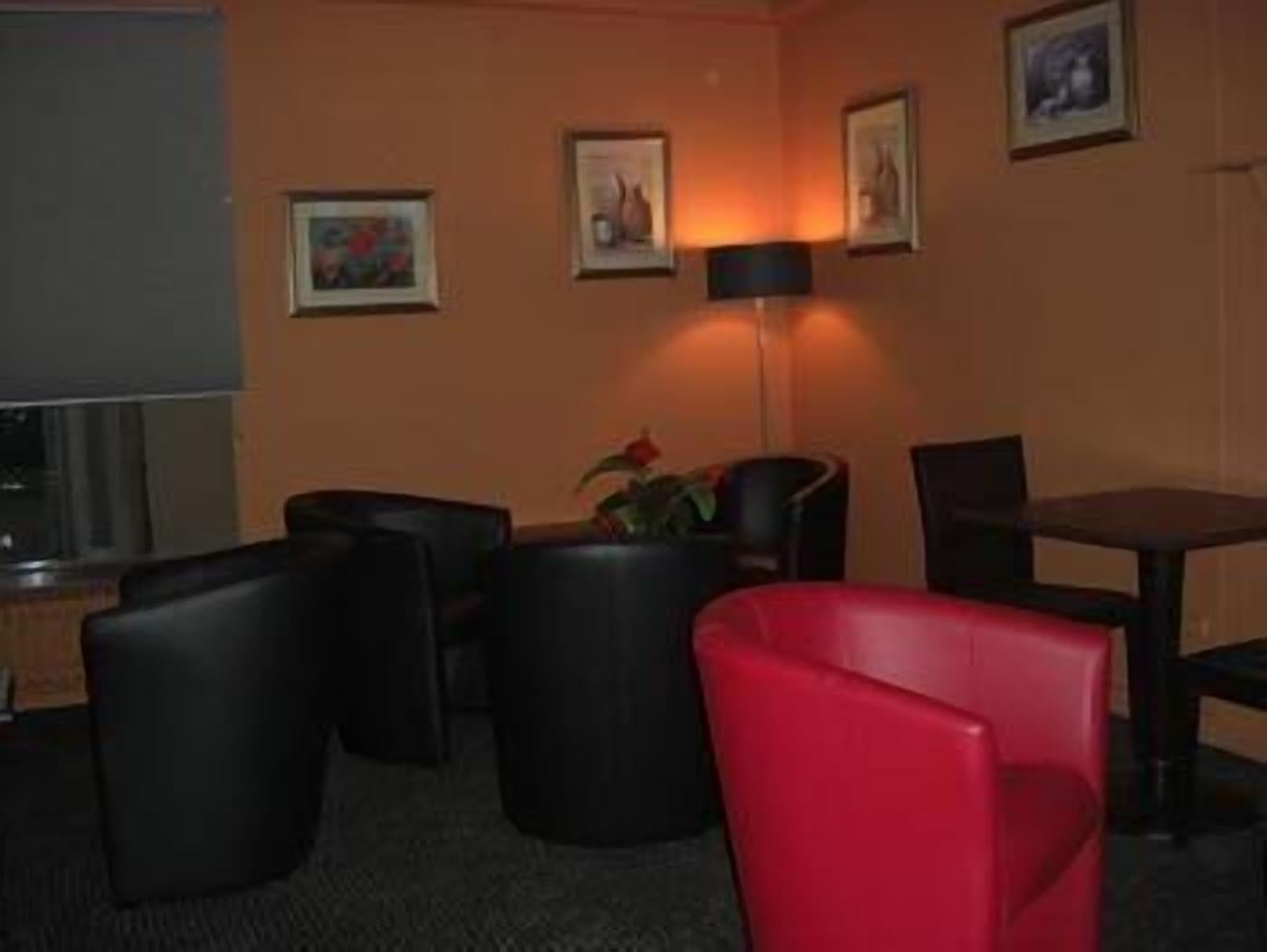 A hotel room with a TV, a sofa, a red chair, and a table.