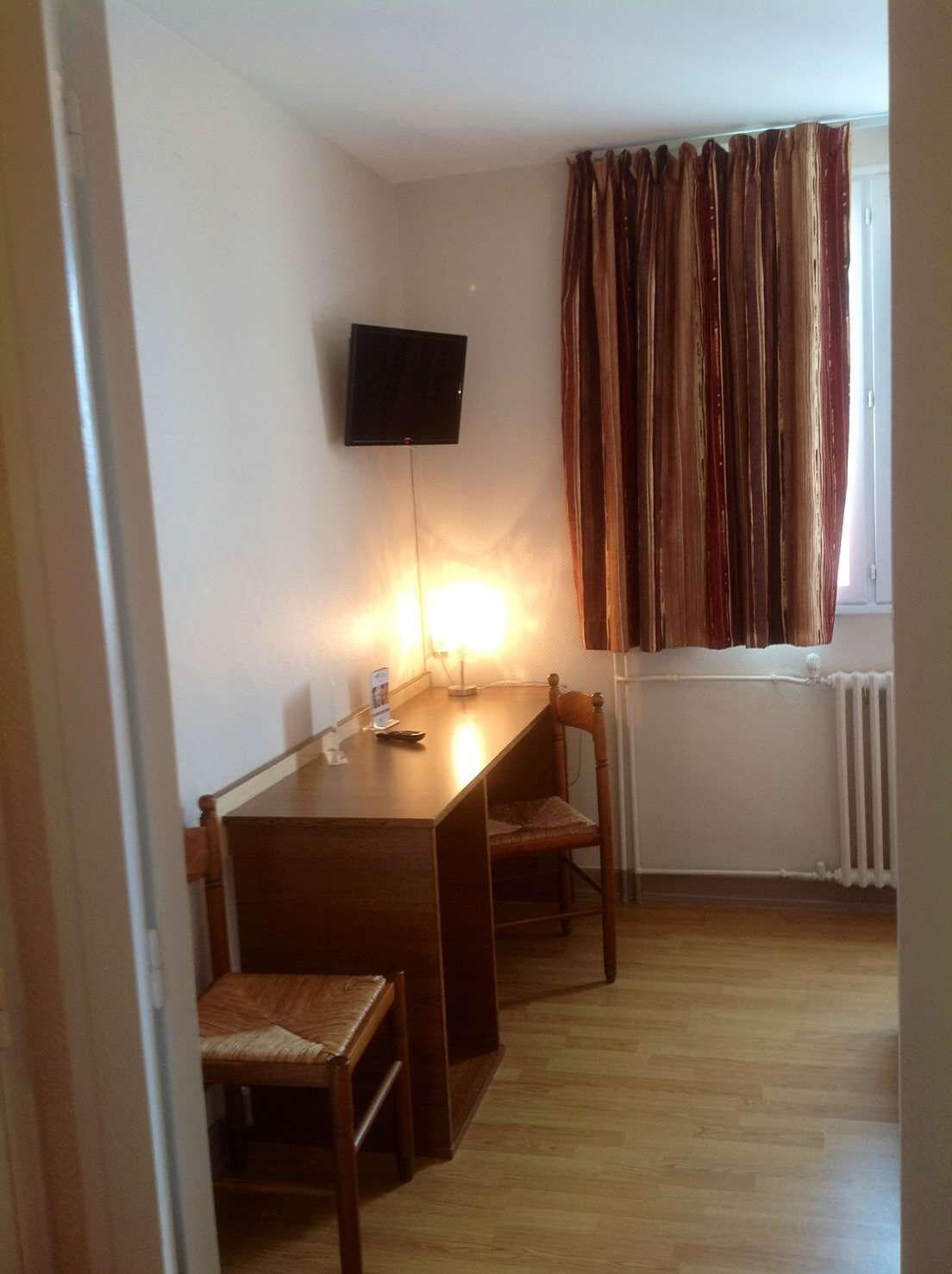 A small room with a wooden table, two chairs, a flat-screen TV mounted on the wall, and a window with curtains.