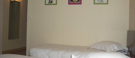 A hotel room with two beds, a door, and three framed pictures on the wall.