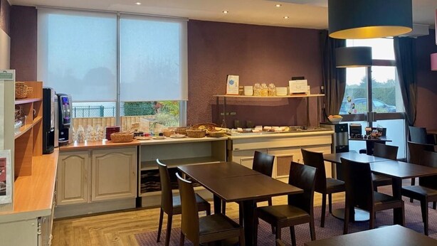 A hotel room with a dining area, a kitchenette, and a large window providing a view of the outdoors. - Brit Hotel le Magdalena (Varennes-Vauzelles)