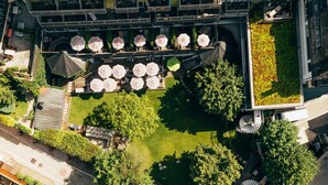 An aerial view of a riverside hotel with outdoor seating areas, a small dock, and a rooftop garden.