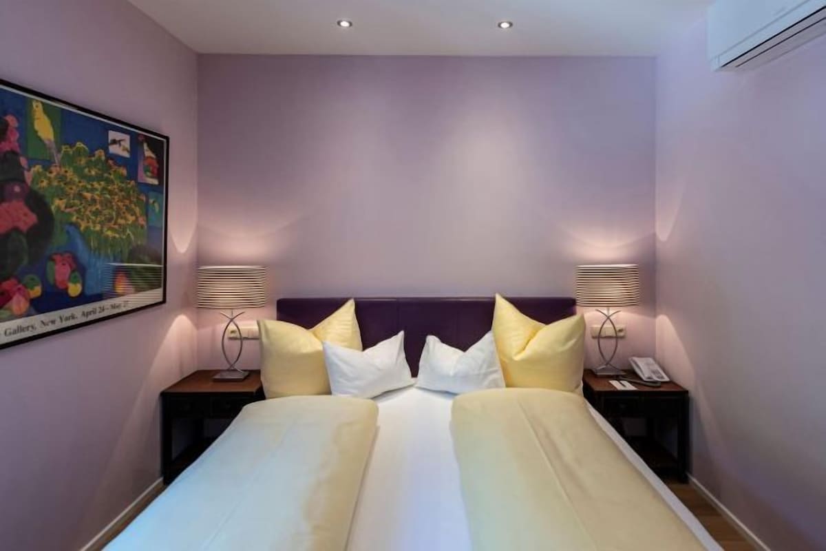 A hotel room with a large bed, two bedside tables, and a painting on the wall.