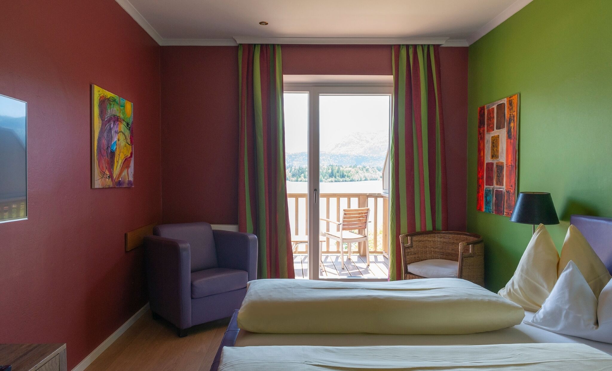 A hotel room with a bed, a chair, a small table, and a balcony with a view.