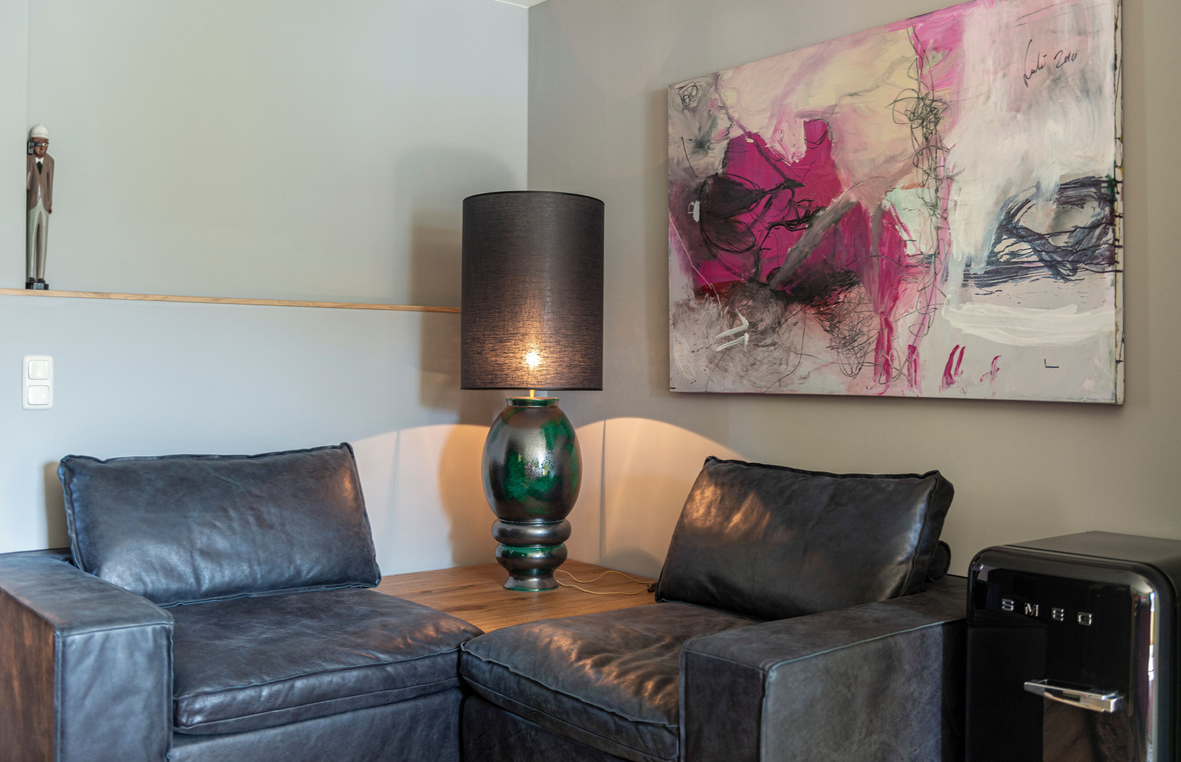 Ein modernes Wohnzimmer mit einem dunkelbraunen Ledersofa, einer grünen Lampe und einem großen abstrakten Gemälde an der Wand.