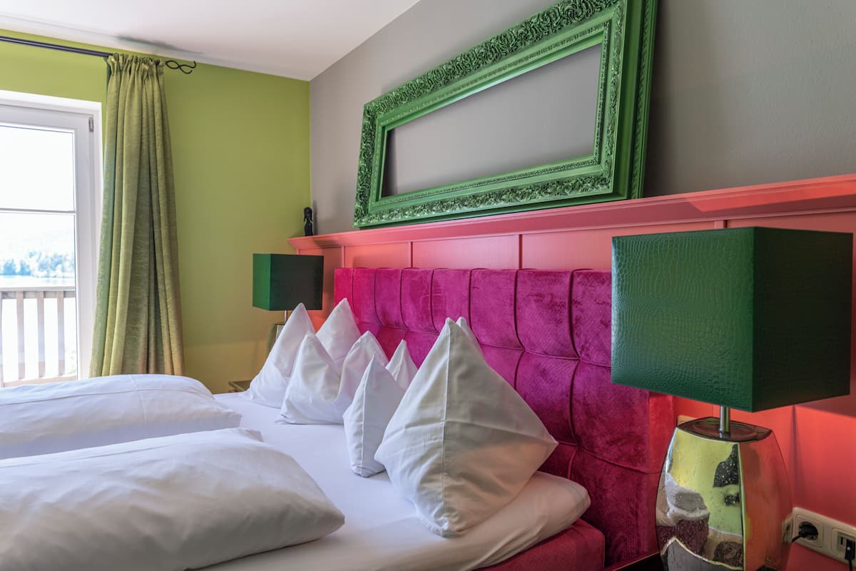 A hotel room with a bed, white pillows, a pink headboard, a green-framed mirror, and a green lamp.