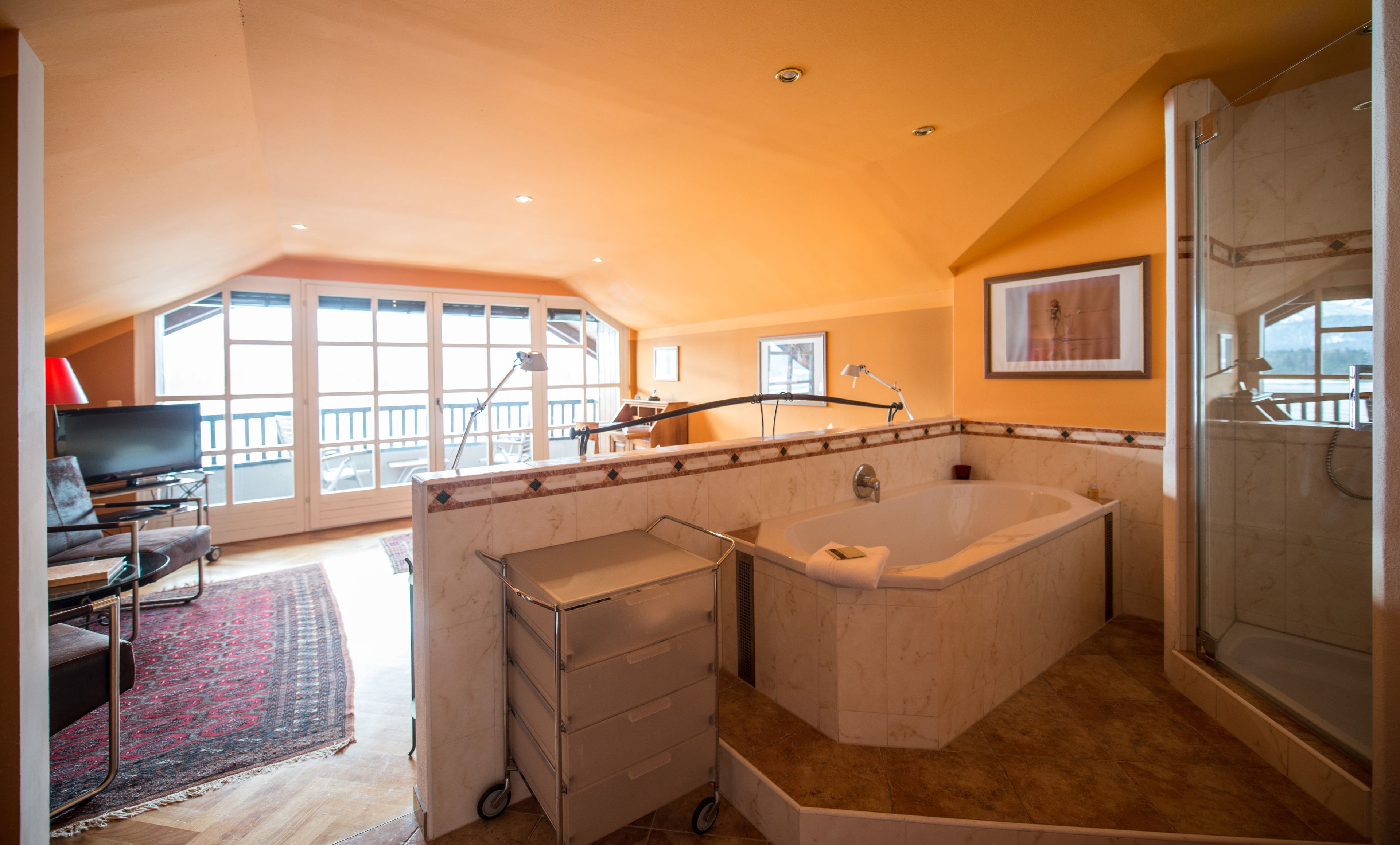 Un baño amplio con una bañera grande, una ducha y un tocador. Hay un balcón con vistas al exterior.