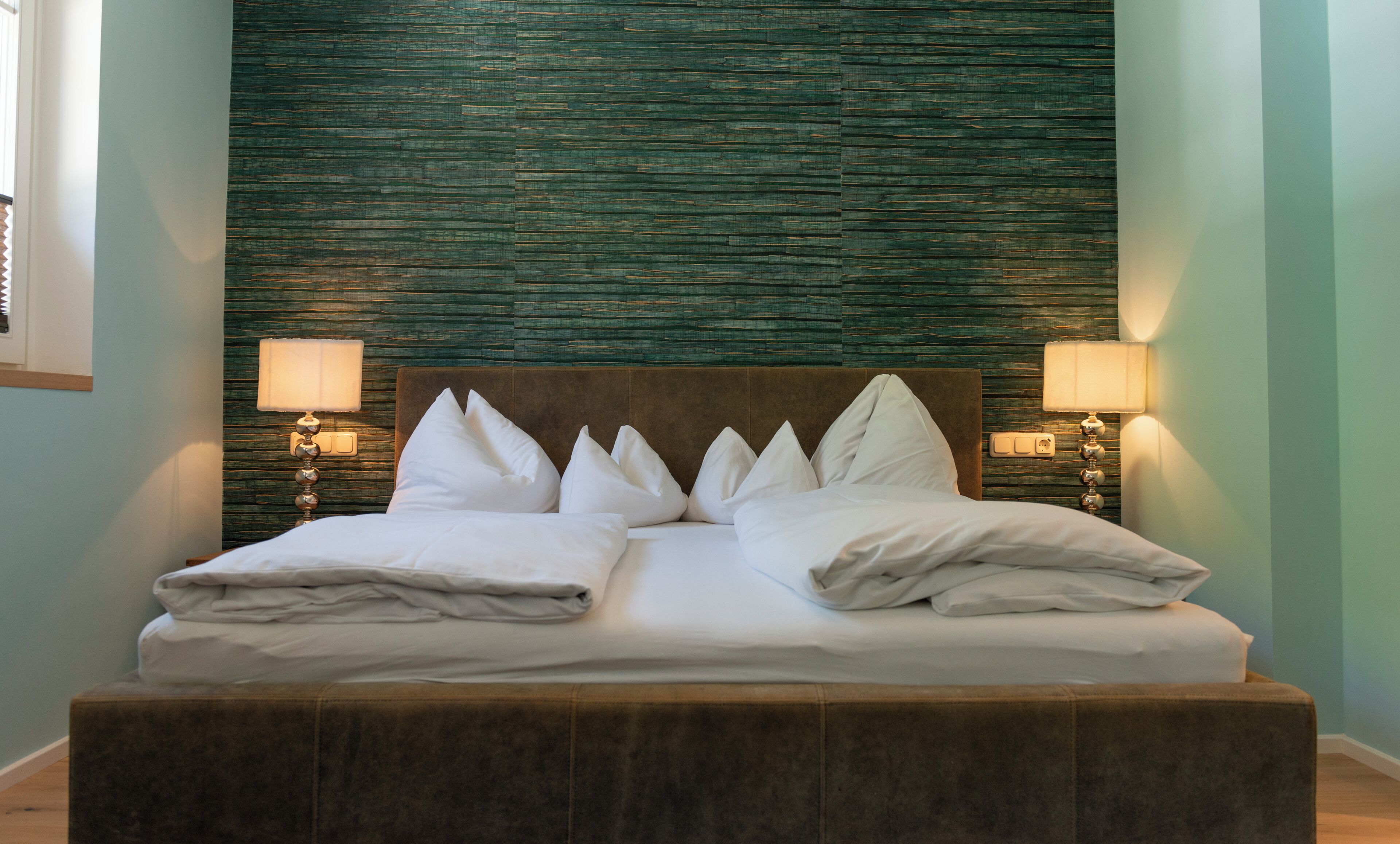 Una cama con sábanas blancas y varios almohadones, un cabecero de madera y dos lámparas adosadas a la pared a cada lado.