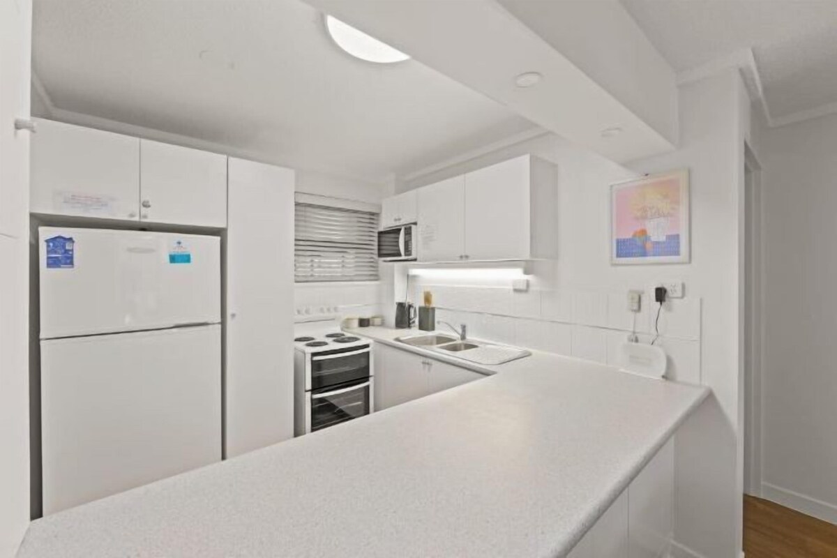 A modern kitchen with white cabinetry, a built-in oven, and a stainless steel sink.
