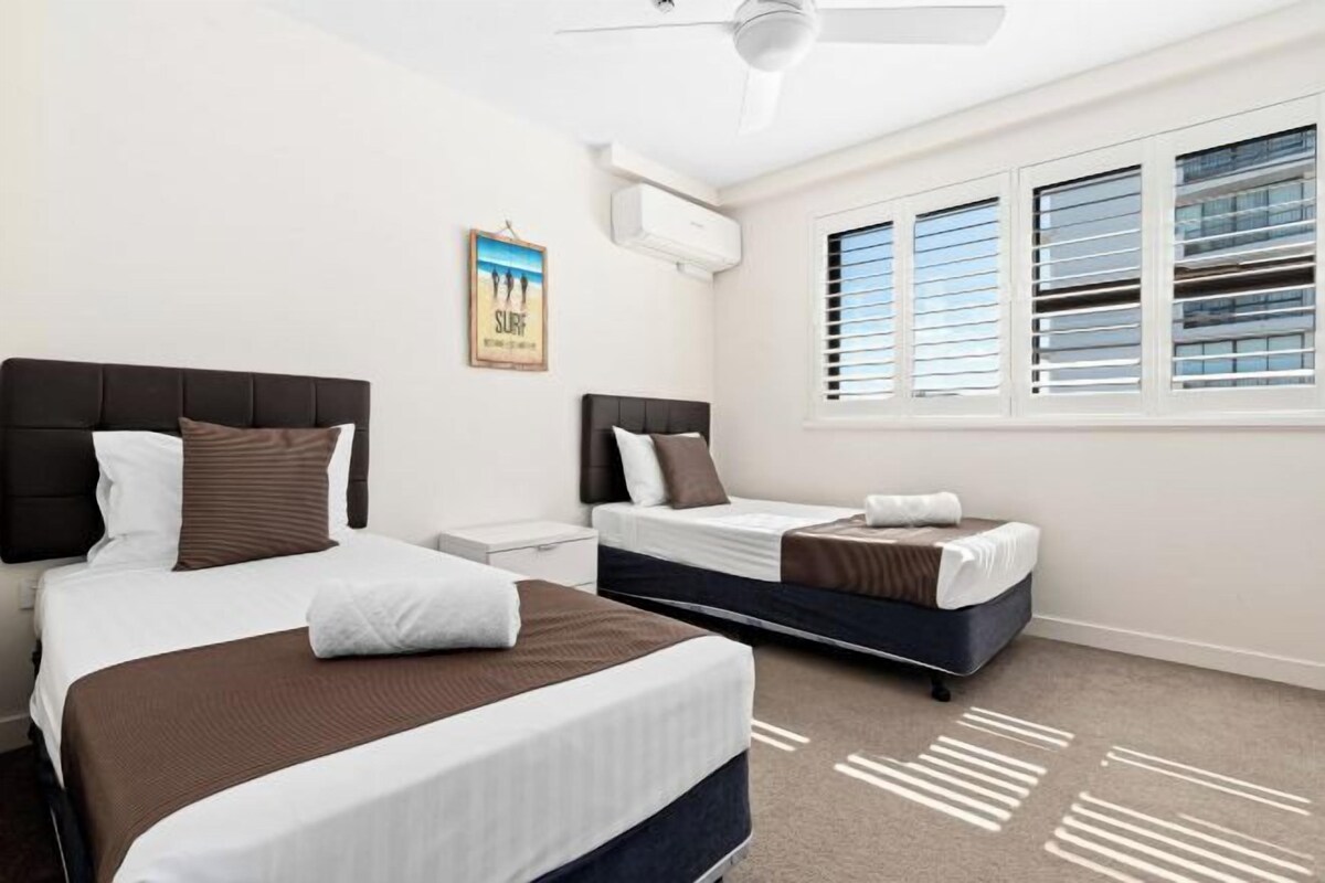 A hotel room with two beds, a ceiling fan, an air conditioning unit, a window with blinds, and a poster on the wall.