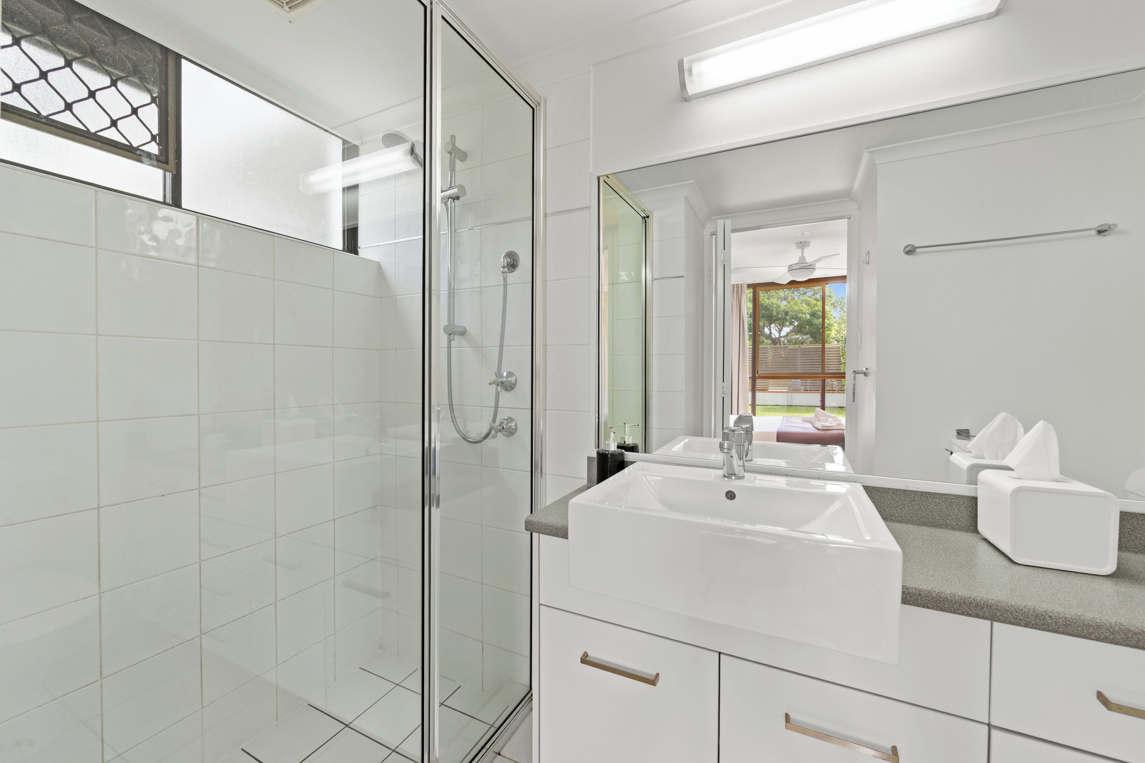 A modern bathroom with a glass-enclosed shower, a white sink, and a large mirror.