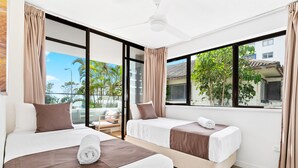 Quarto de hotel com duas camas, janelas amplas, ventoinha no teto e vista para o exterior.