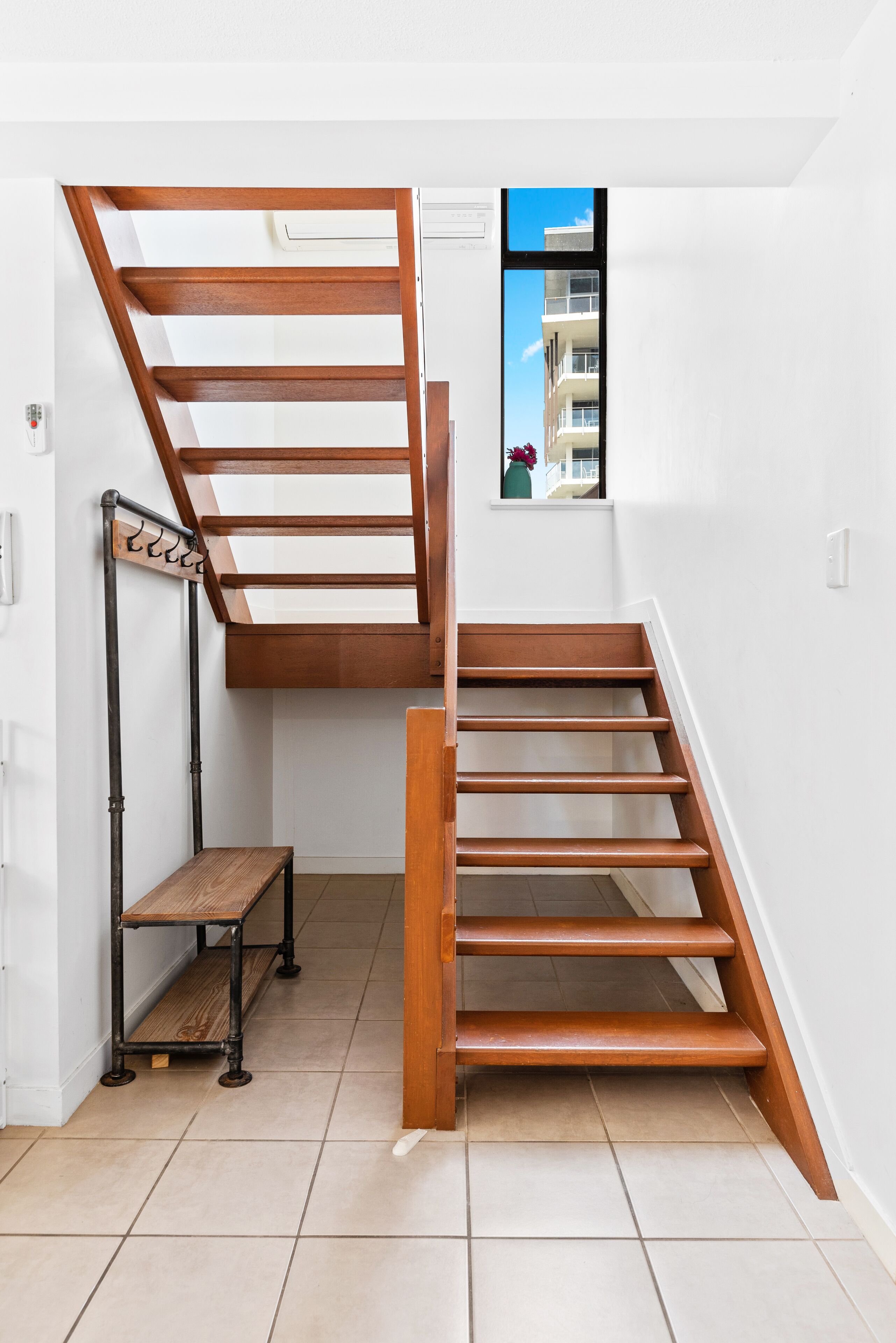 A staircase with a wooden finish, a small bench, and a window with a view of a building.