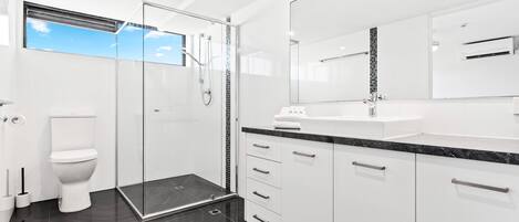 Un baño moderno con ducha envuelta en vidrio, inodoro blanco y un espejo grande sobre el lavamanos.