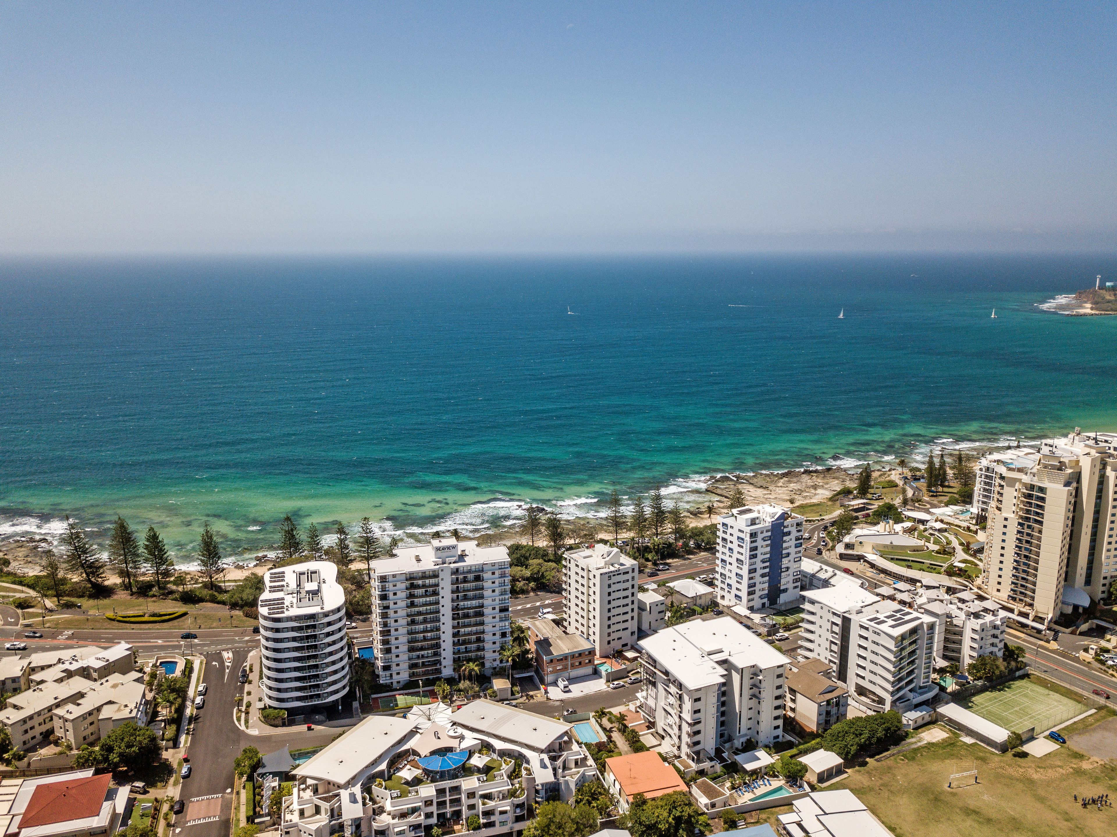 Un paisaje urbano costero con edificios altos, un mar azul y despejado y una carretera con vehículos.