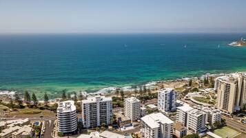 Un paisaje urbano costero con edificios altos, un mar azul y despejado y una carretera con vehículos.
