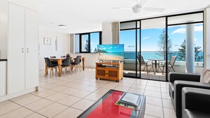 Uma sala de estar moderna com televisão, área de jantar e varanda com vista para o oceano.