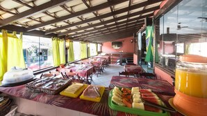 A restaurant with a covered outdoor seating area, tables with yellow curtains, and a buffet with various food items. - Meu Sonho Pousada (Búzios)
