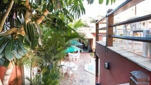 A staircase leading to a terrace with outdoor seating, surrounded by lush greenery and a stone wall. - Meu Sonho Pousada (Búzios)