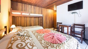 A hotel room with a wooden ceiling, a bed with patterned bedding, a desk with a chair, and a flat-screen TV mounted on the wall. - Meu Sonho Pousada (Búzios)