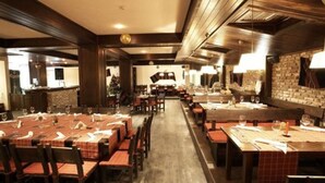 A restaurant with multiple tables and chairs, a brick wall, and a long counter. - Vihren Palace Ski & Spa Resort (Bansko)