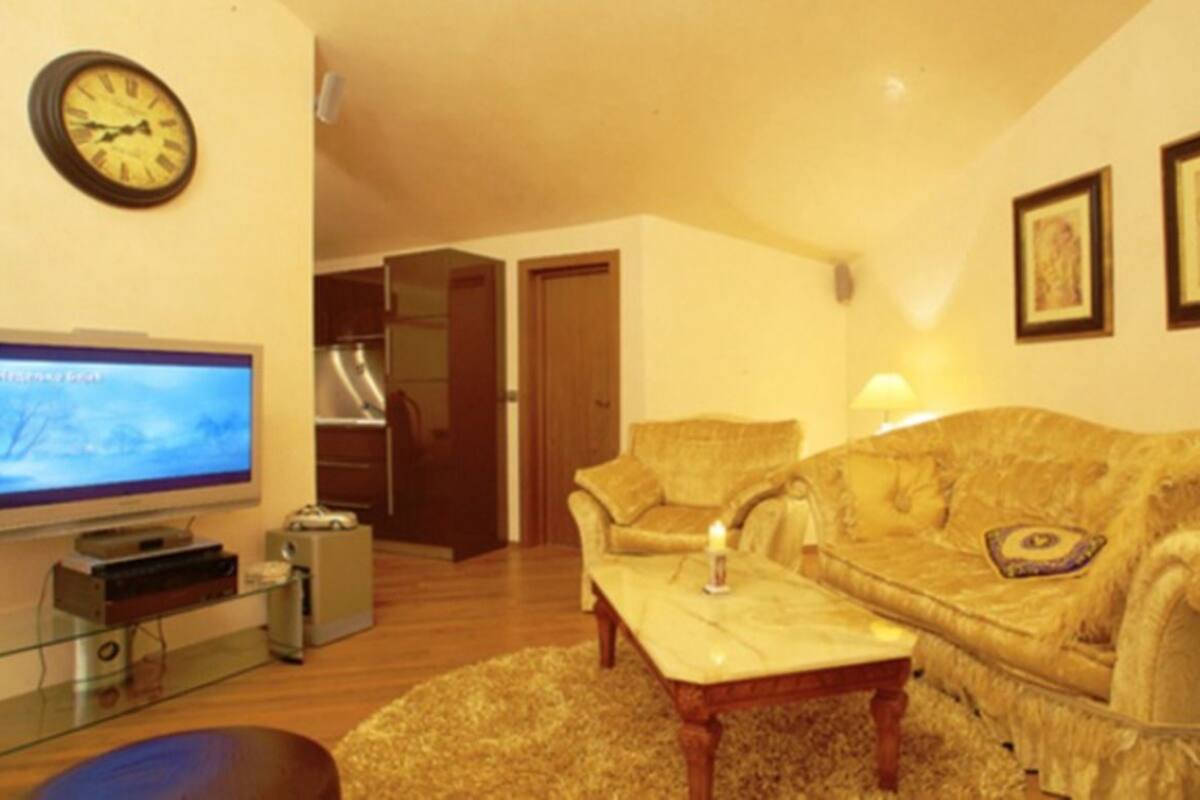Uma sala de estar com televisão, sofá, poltrona, mesa de centro e abajur.
