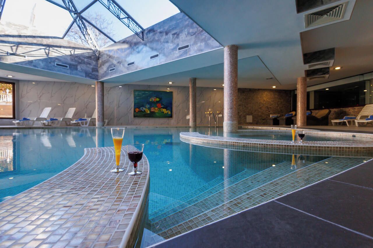 An indoor swimming pool with lounge chairs and a glass of wine on the edge.