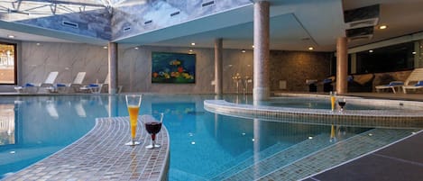 An indoor swimming pool with lounge chairs and a glass of wine on the edge.