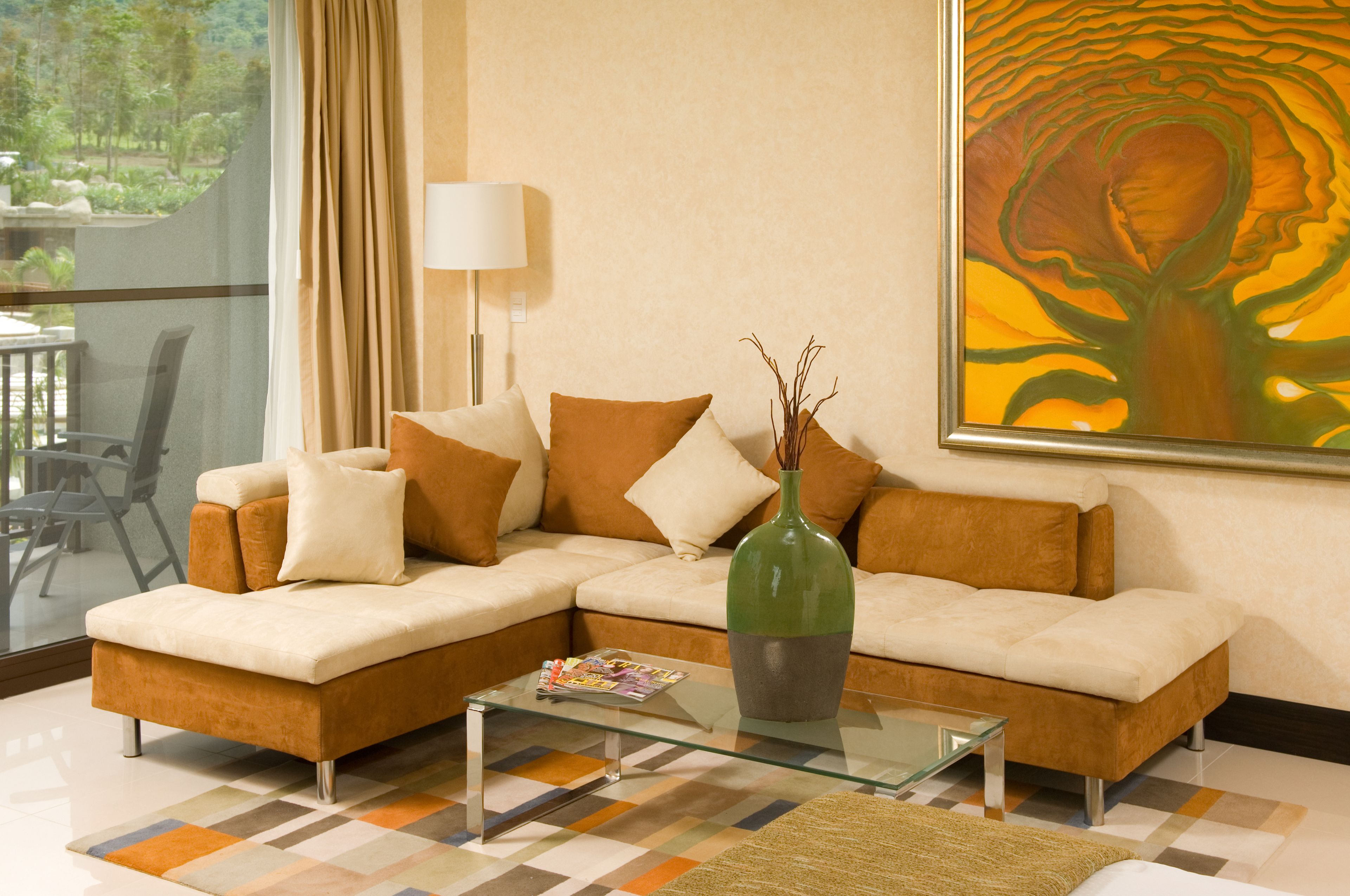 A modern living room with a sectional sofa, a glass coffee table, and a large abstract painting on the wall.