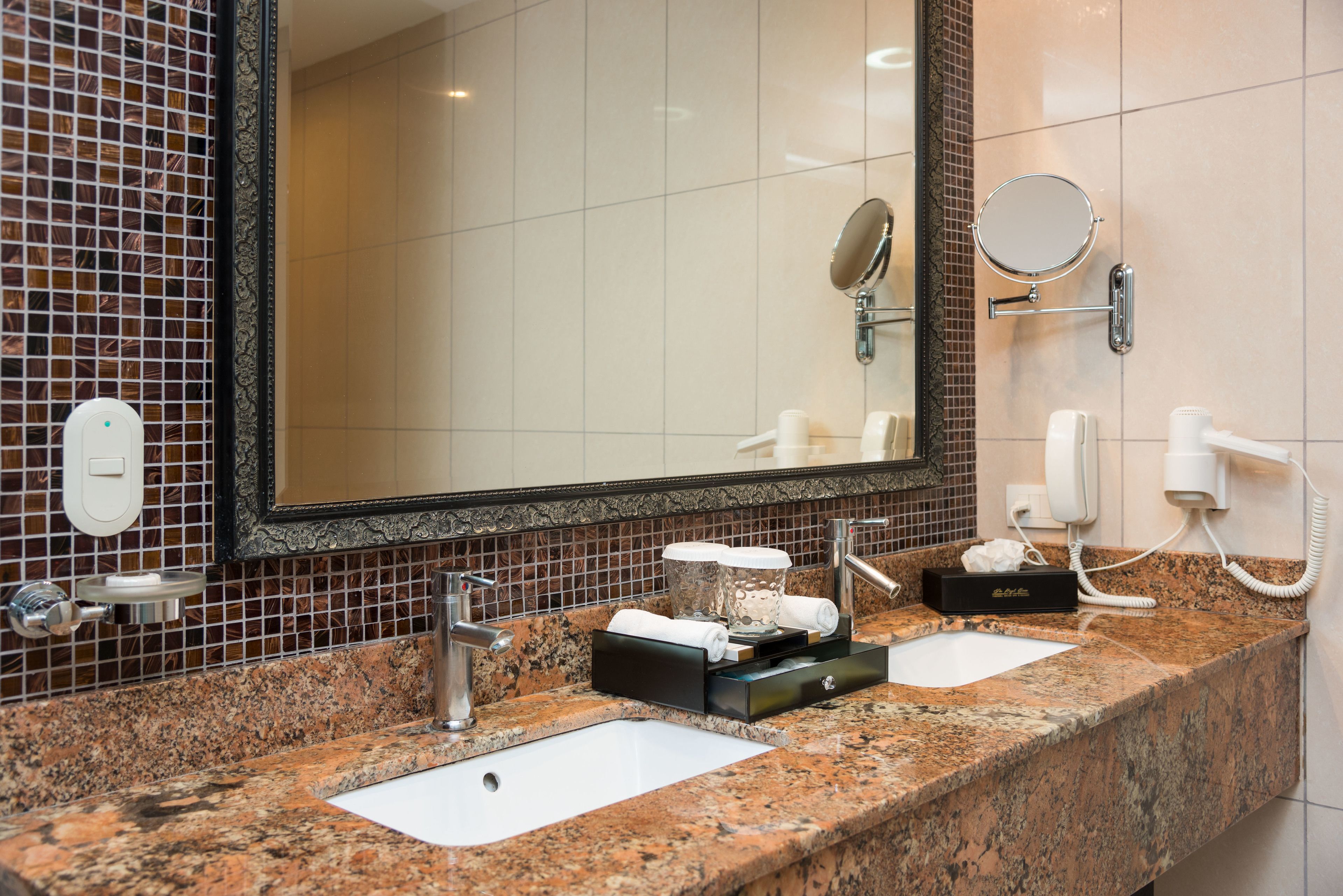 A bathroom with two sinks, a large mirror, a telephone, and a towel warmer.