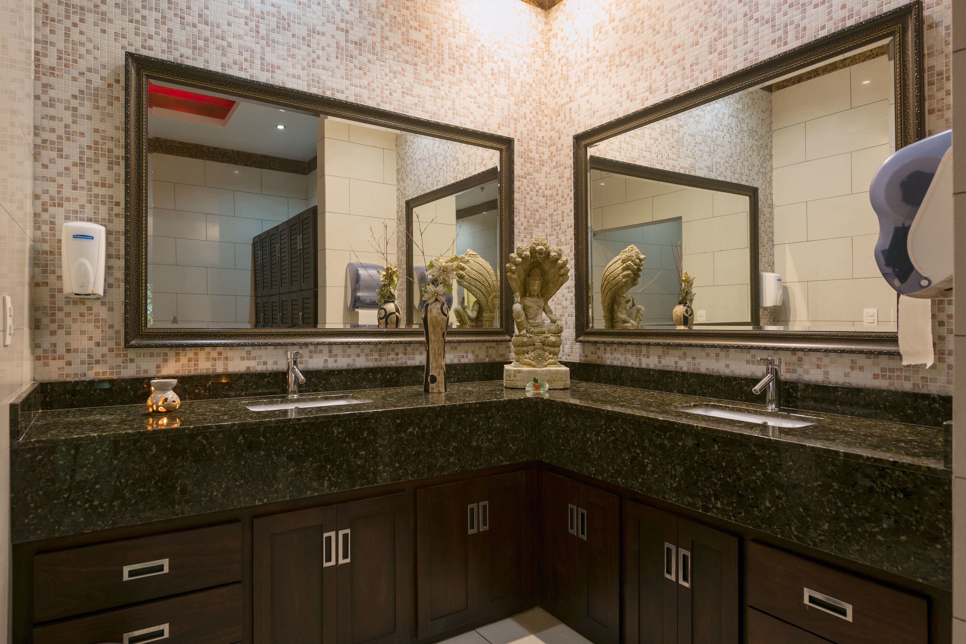 A bathroom with two large mirrors, dark wooden cabinets, a granite countertop, and a decorative plant.